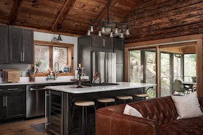 A kitchen with a central island, bar stools, a brown leather couch, and large windows.