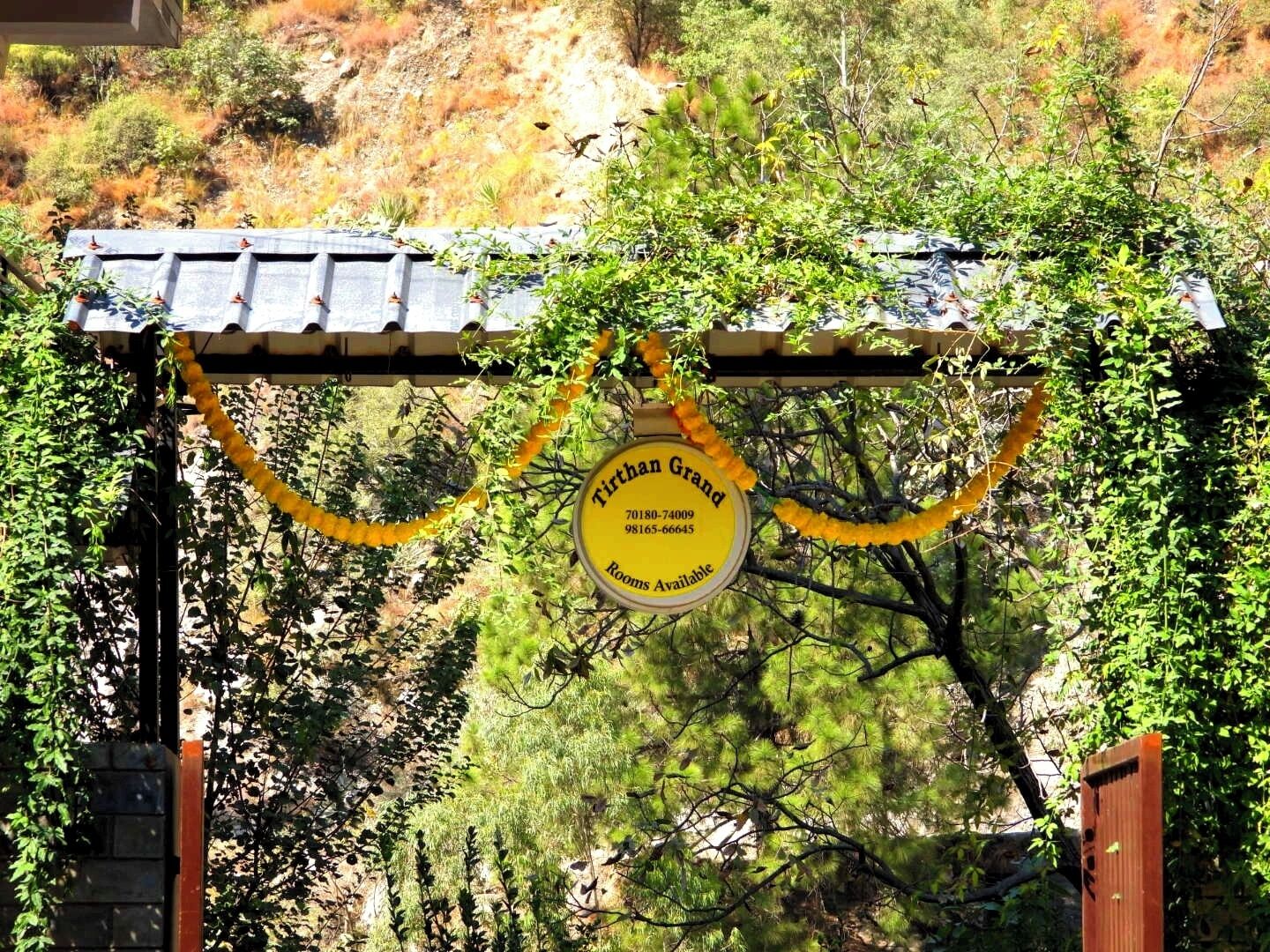A yellow sign with contact details for Tirthan Grand, indicating rooms are available.