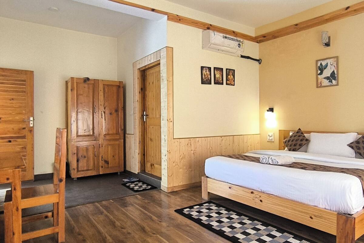A room with a wooden bed, a desk, and a wardrobe. There are wall-mounted lights and a picture frame on the wall.
