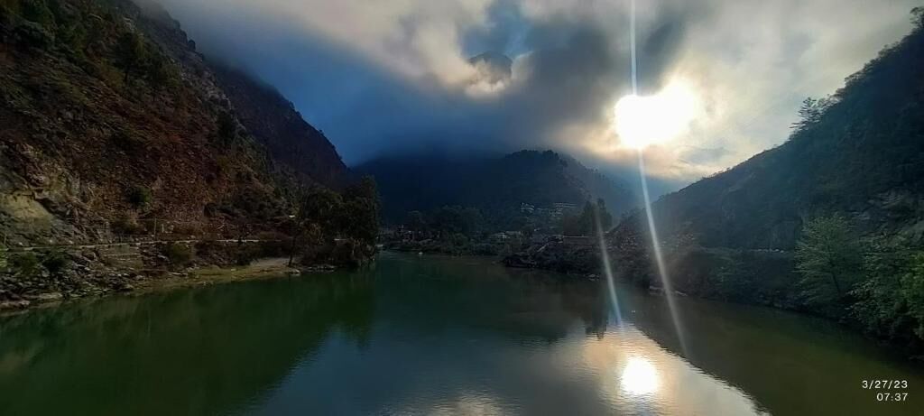 A river surrounded by mountains with a clear sky and sunlight.