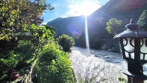 A river flowing through a valley with a mountain backdrop and a lamp post in the foreground. - Tirthan Grand Riverside  (Sainj)