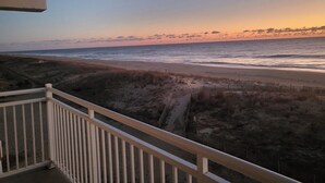 En balkon med udsigt over en strand i solnedgang.