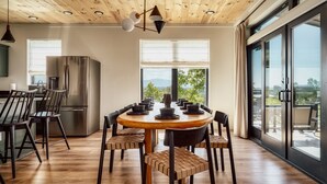 A modern kitchen with a dining area, large windows, and a view of the outdoors.