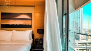 Hotellihuone, jossa on sänky, yöpöytä, lamppu, taulu ja suuri ikkuna, josta avautuu näkymä kaupunkiin.