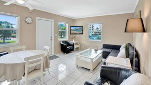 Ein modernes Wohnzimmer mit Essbereich, Deckenventilator, Fernseher und Blick auf einen Pool durch die Fenster.
