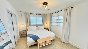 A spacious bedroom with a large bed, bedside tables, a bench, and two windows with curtains. - Beautiful 3 2 Home in Pompano Beach - Close to Beach (Pompano Beach)