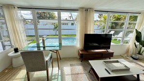 A living room with a glass table, a TV, and a view of a swimming pool. - Beautiful 3 2 Home in Pompano Beach - Close to Beach (Pompano Beach)