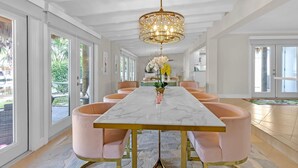 A dining area with a marble table, pink chairs, and a chandelier. - Flirty Flamingo Colorful Waterfront Escape w Pool (Wilton Manors)