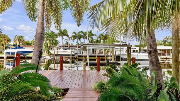 A wooden dock leading to a marina with boats, surrounded by palm trees and water. - Flirty Flamingo Colorful Waterfront Escape w Pool (Wilton Manors)