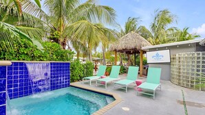 A pool area with a blue tiled edge, lounge chairs, and a thatched-roof structure. - Flirty Flamingo Colorful Waterfront Escape w Pool (Wilton Manors)