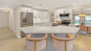 A modern kitchen with white cabinetry, stainless steel appliances, and a central island with bar stools. - Flirty Flamingo Colorful Waterfront Escape w Pool (Wilton Manors)
