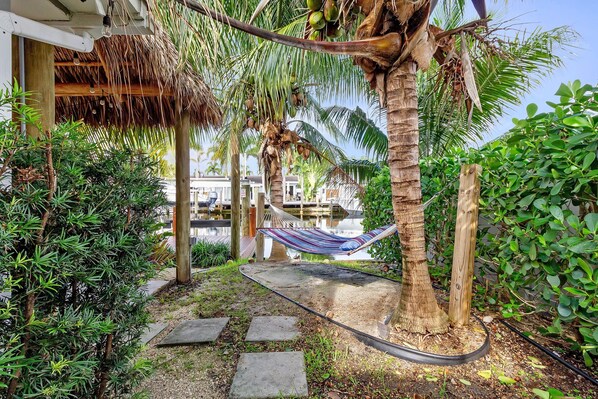 A hammock under a palm tree, a thatched roof structure, and a pathway leading to a building.