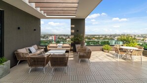Una terraza en la azotea con mobiliario exterior, vistas a la ciudad y una pérgola.