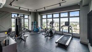 Un gimnasio con diversos equipos de ejercicio, amplias ventanas y vista a la ciudad.