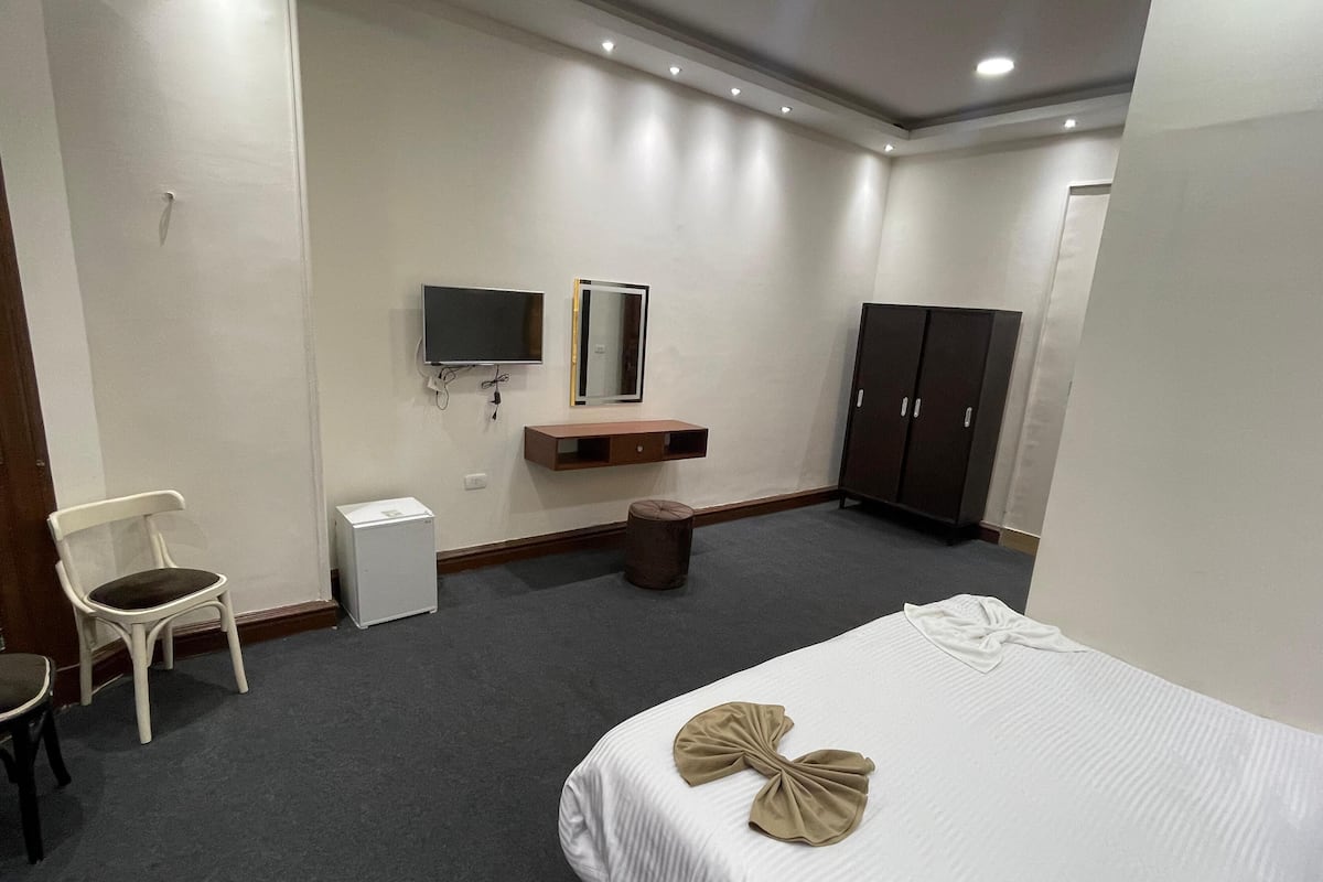 Une chambre d’hôtel avec un lit, une chaise, une télévision, une armoire et une petite table.