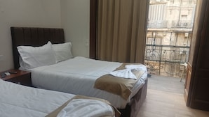 Een hotelkamer met twee bedden, een nachtkastje en uitzicht op een balkon met een smeedijzeren balustrade.