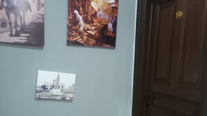Een hal met drie ingelijste foto's aan de muur, een houten deur met koperen handgreep en een betegelde vloer.