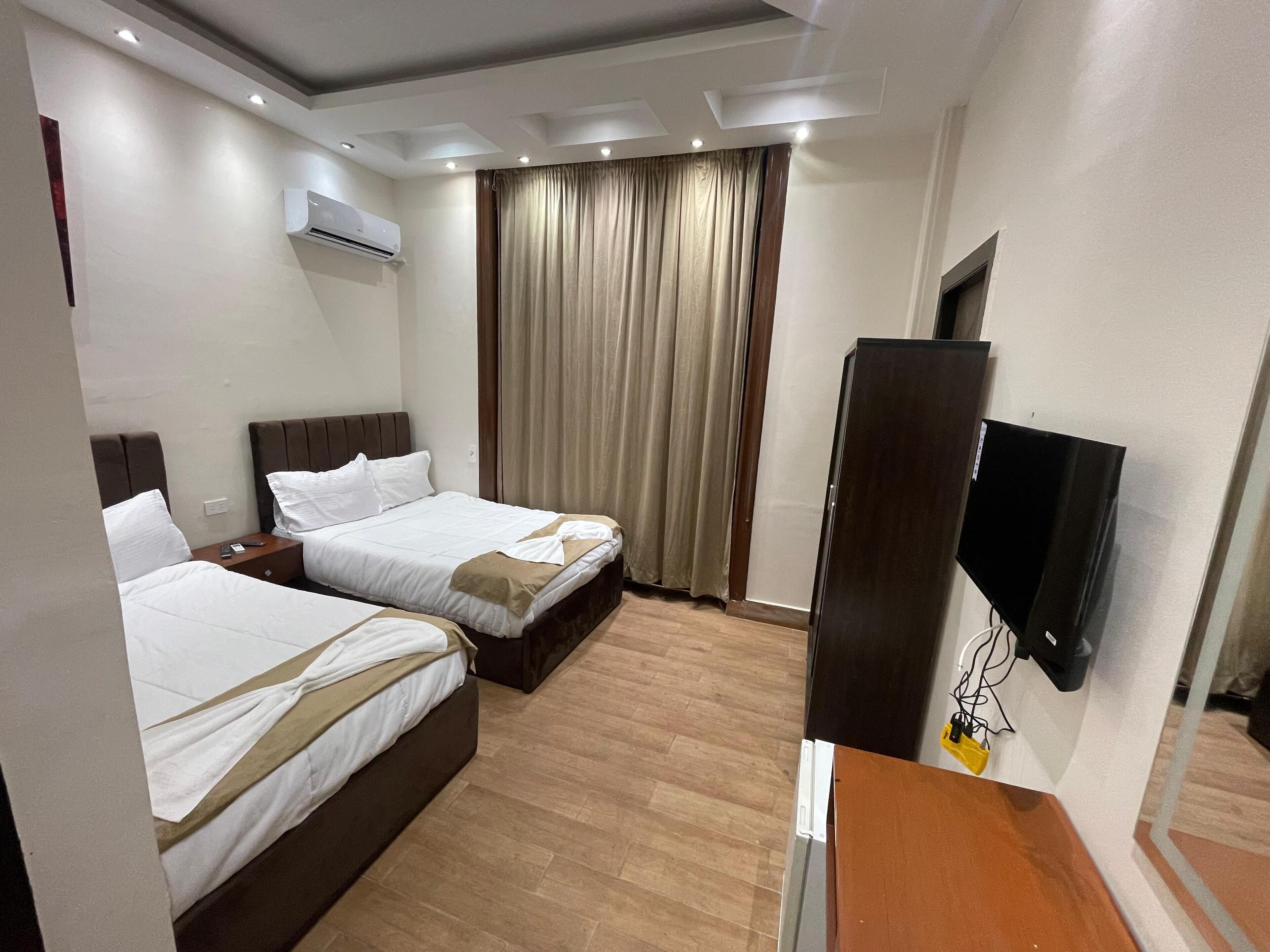 A hotel room with two beds, a flat-screen TV, and an air conditioning unit.