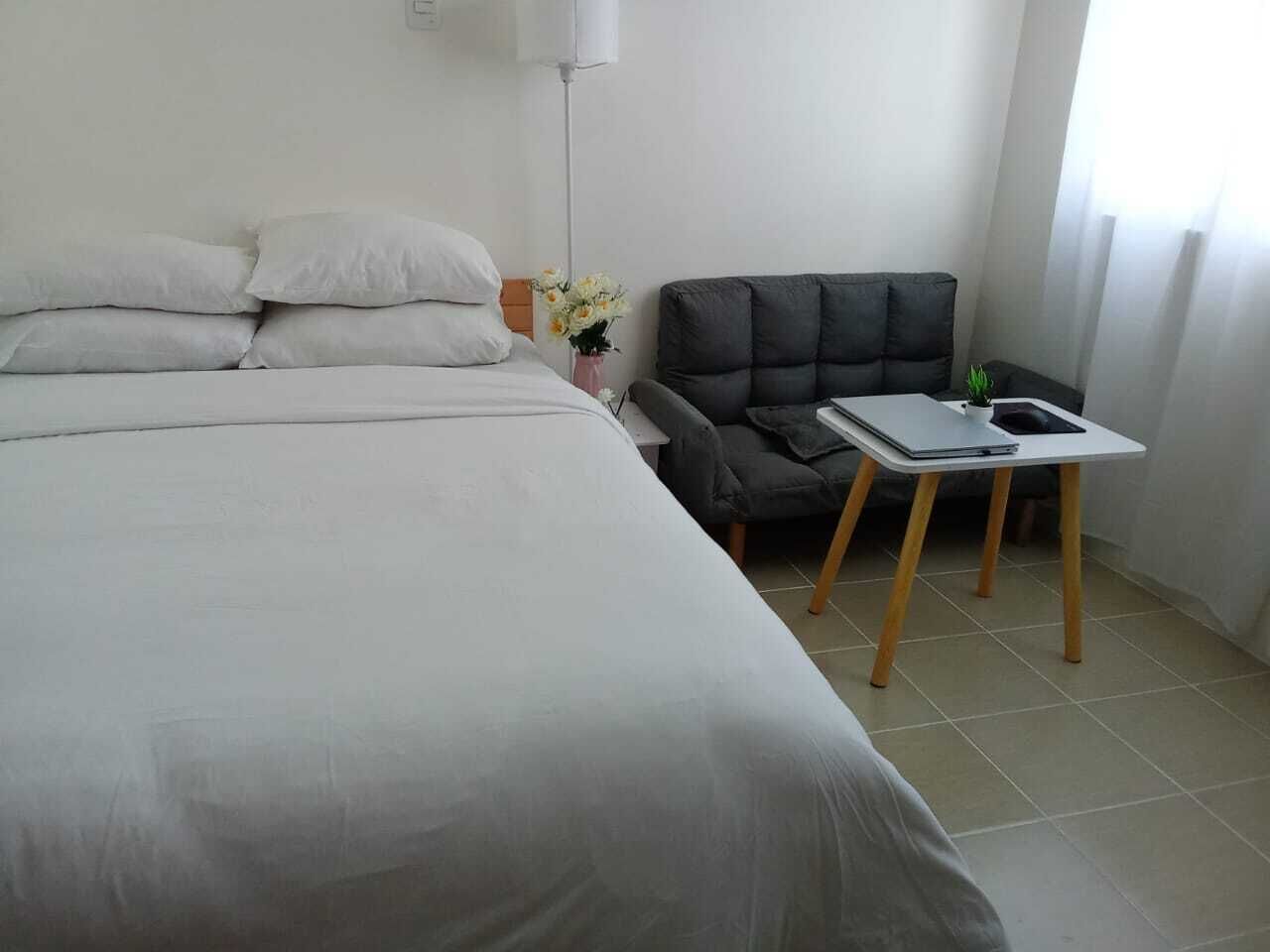 A bedroom with a bed, a chair, a small table, and a nightstand.