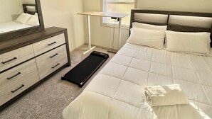 Une chambre à coucher comprenant un lit, une commode, un miroir, un tapis de course et une fenêtre avec des stores.