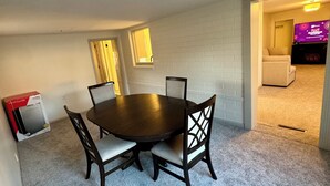 Un coin repas avec une table ronde et quatre chaises, un sol recouvert d’une moquette et un téléviseur en arrière-plan.