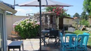 Une terrasse extérieure avec une table et des chaises, un mur en pierre et un arbuste fleuri.