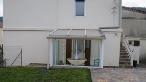 Un bâtiment doté d’une entrée avec une porte en verre, d’un petit patio avec une table et des chaises, et d’un escalier menant à un étage supérieur.