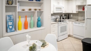 A modern kitchen with white cabinetry, a stainless steel stove, and a white dining table with chairs. - Walk to Wilton Drive - Spacious Quiet Villa 1 (Wilton Manors)
