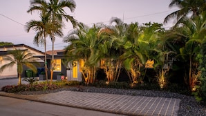 A modern house with a paved driveway, surrounded by lush greenery and palm trees. - Walk to Wilton Drive - Spacious Quiet Villa 1 (Wilton Manors)
