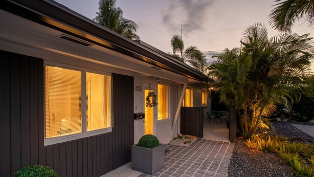 A modern house with a paved driveway, large windows with blinds, and a well-maintained garden with palm trees and shrubs. - Walk to Wilton Drive - Spacious Quiet Villa 1 (Wilton Manors)