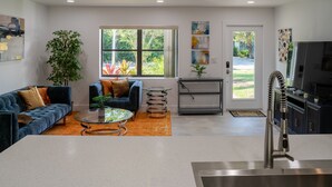 A modern living room with a sofa, coffee table, and a kitchen area with a sink and refrigerator. - Spacious 3BR Home 2 Baths Amazing Pool Area (Wilton Manors)