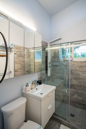 Un baño moderno con ducha de vidrio, un lavabo blanco y un espejo grande sobre el mueble.