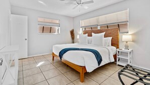 A bedroom with a bed, a ceiling fan, a bedside table with a lamp, and a window with blinds. - Citrus Isles Waterfront Home (Fort Lauderdale)