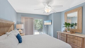 A bedroom with a bed, a ceiling fan, a TV, a dresser, and a large mirror.