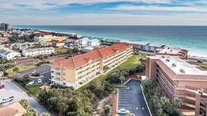 A coastal hotel with multiple buildings, a parking lot, and a view of the ocean.