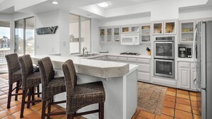 A modern kitchen with white cabinetry, a large island, and a dining area with wicker chairs.