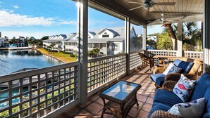A covered outdoor area with a view of a lake, a ceiling fan, wicker furniture, and a glass table.