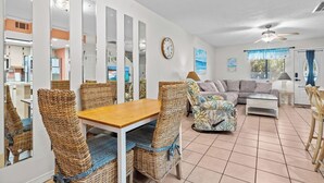 A spacious living area with a dining table, wicker chairs, a sofa, and a ceiling fan.