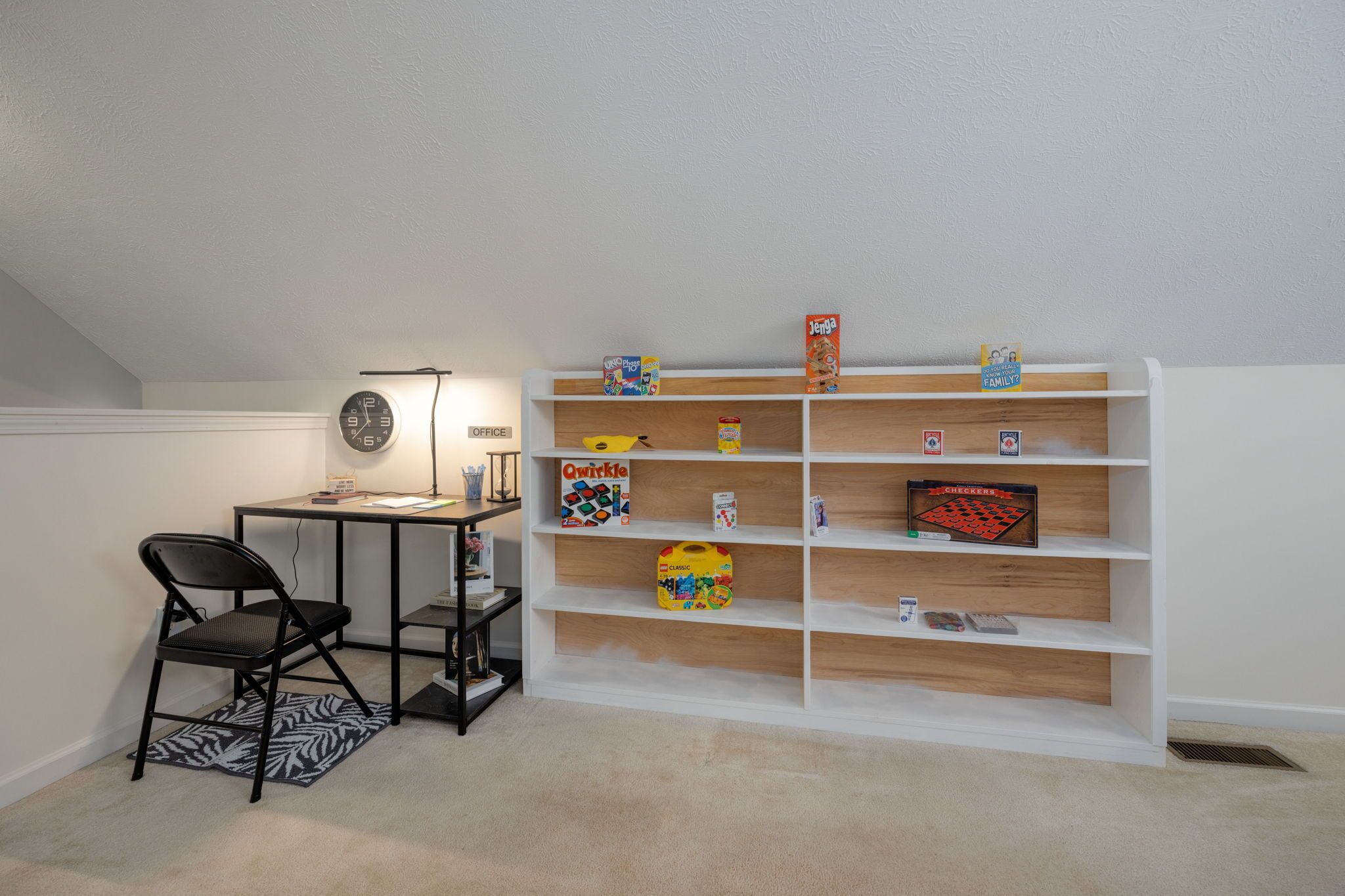 A room with a desk, chair, and a white bookshelf with various items.