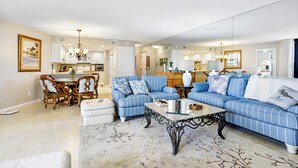 A living room with a blue-striped sofa, a coffee table, and a dining area with wooden chairs and a chandelier.