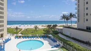 A pool area with blue lounge chairs, a circular pool, and a view of the beach and ocean.