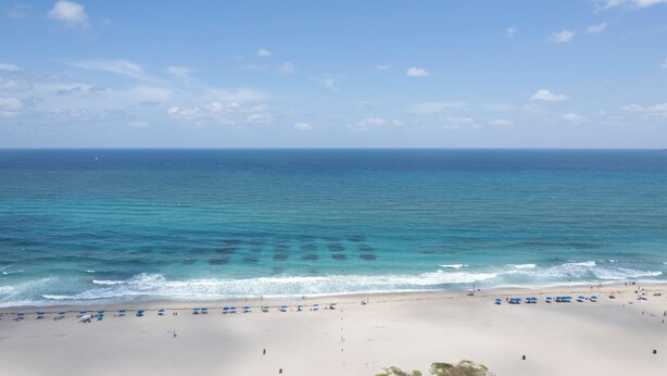 A beach with a clear view of the ocean, a sandy shore, and a few umbrellas.