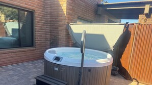 Un bain à remous avec des marches et un couvercle, entouré d’un mur de briques et d’une clôture en bois.
