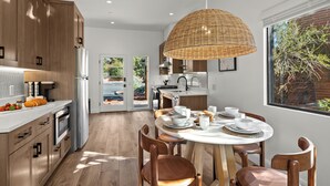 Une cuisine moderne avec des meubles en bois, un coin repas doté d’une table ronde et de chaises, et un grand luminaire suspendu en osier.