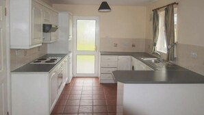 Una cocina compacta con gabinetes blancos, estufa, lavamanos y ventana con cortinas.