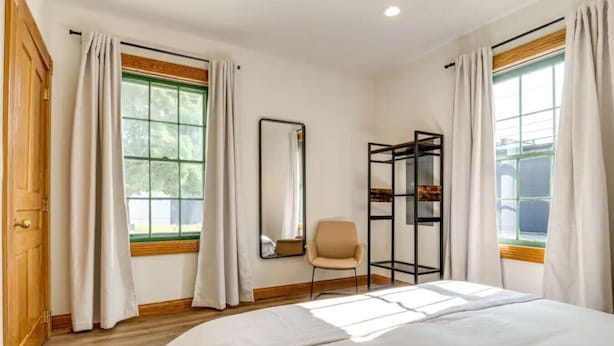 Ein Schlafzimmer mit einem großen Bett, einem Sessel, einem Spiegel und einer schwarzen Regaleinheit.