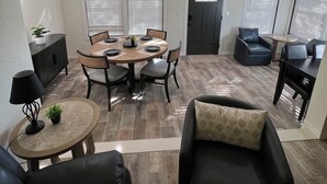 A spacious living area with a dining table, chairs, a sofa, and a small side table with a lamp.