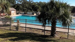 A swimming pool surrounded by a fence, with palm trees and a building in the background.