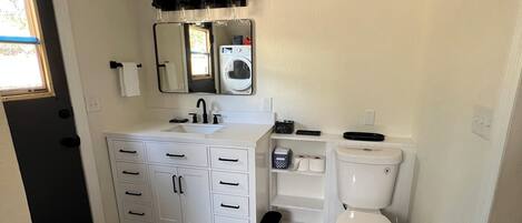 A bathroom with a patterned tile floor, a white sink with a mirror above it, a toilet, and a black trash bin.