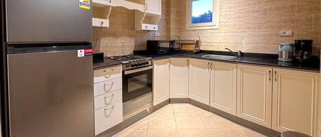 A modern kitchen with a stainless steel refrigerator, gas stove, oven, and white cabinets.